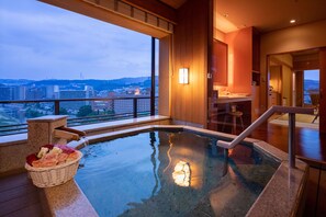 A hot tub with a view of a cityscape, a wooden bench, and a basket of flowers. - Hotel Wakamizu (Takarazuka)