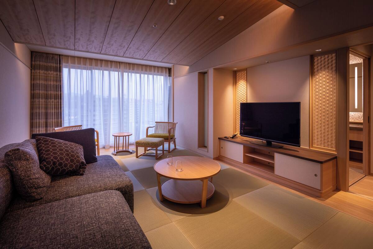 A modern living room with a sofa, a coffee table, a TV, and a seating area with chairs.