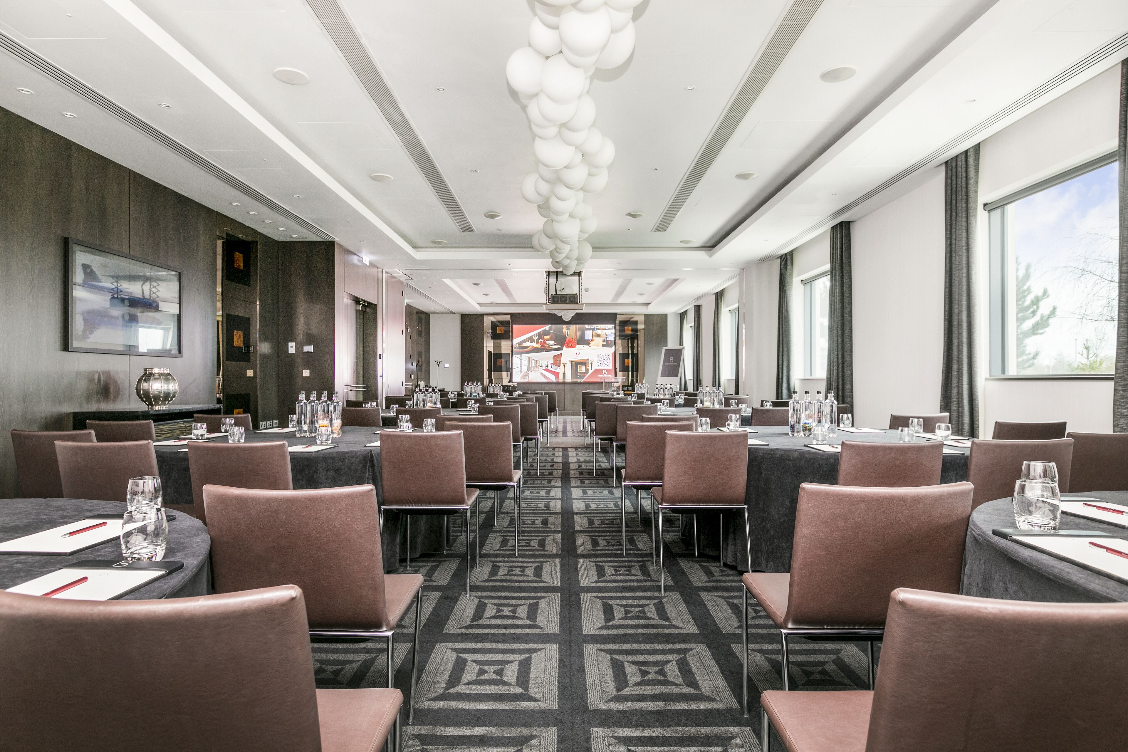 A conference room with multiple tables and chairs, a patterned carpet, and a modern ceiling design.