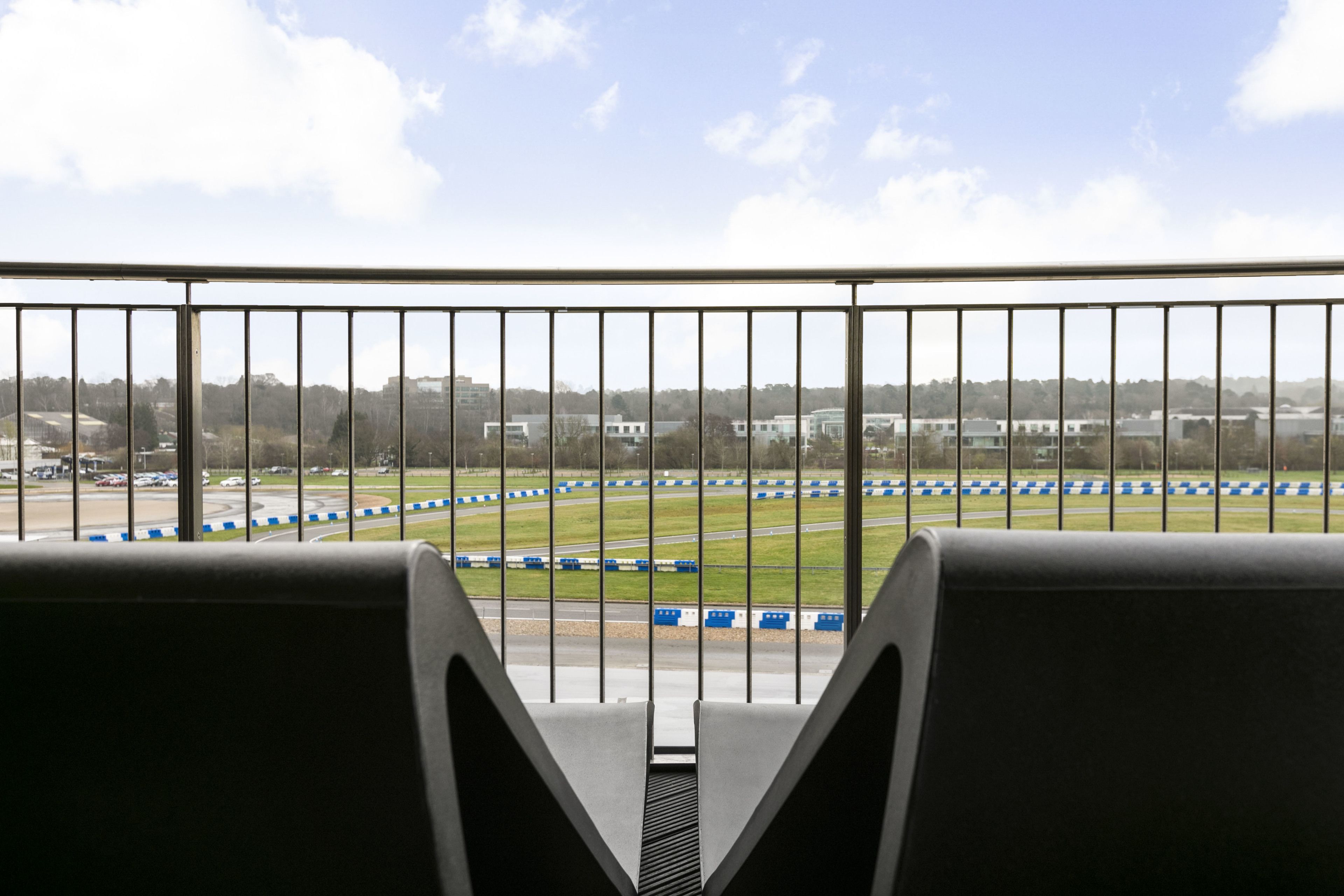 A view from a balcony with a metal railing, overlooking a race track with blue and white barriers.