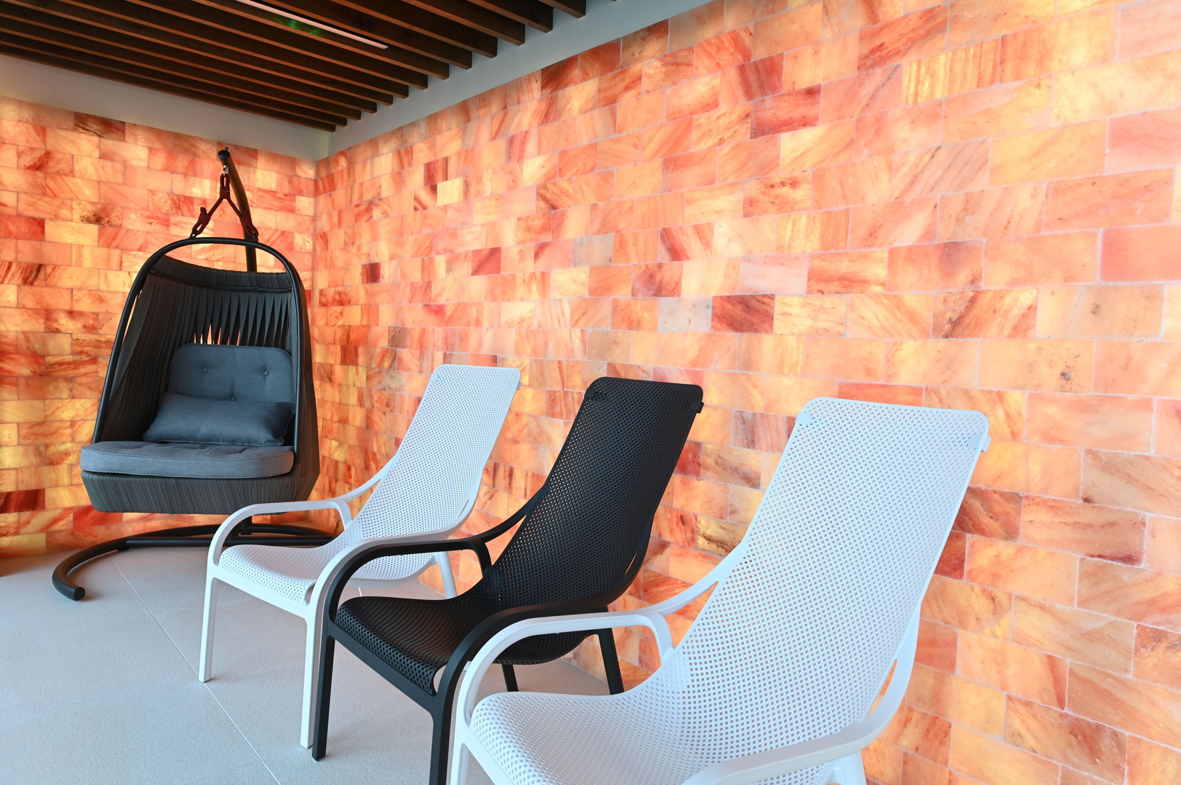 Una habitación con una silla colgante, dos sillones y una pared con textura.