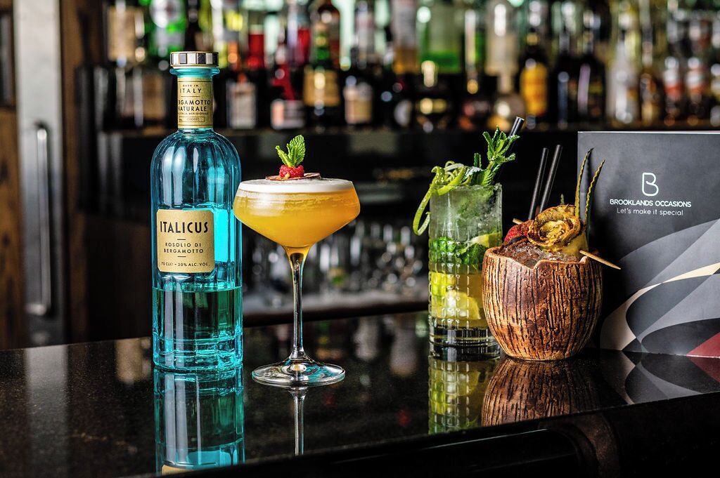 Um bar com uma garrafa de licor italiano, um copo de martini e um drink em uma casca de coco.