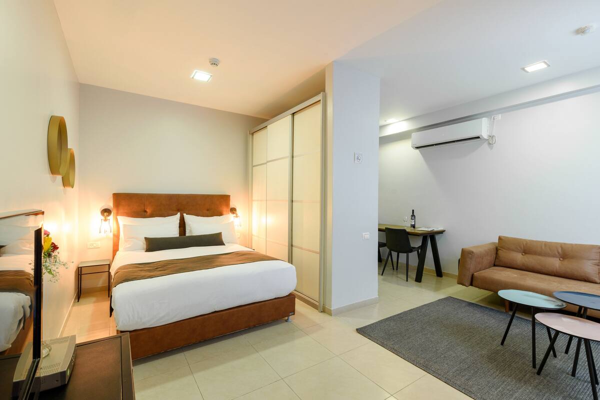 A modern hotel room with a large bed, a sofa, a small table, and a desk.