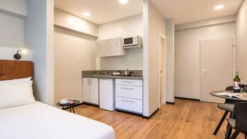 A hotel room with a bed, a small kitchenette, a dining area with a table and chairs, and a separate door.