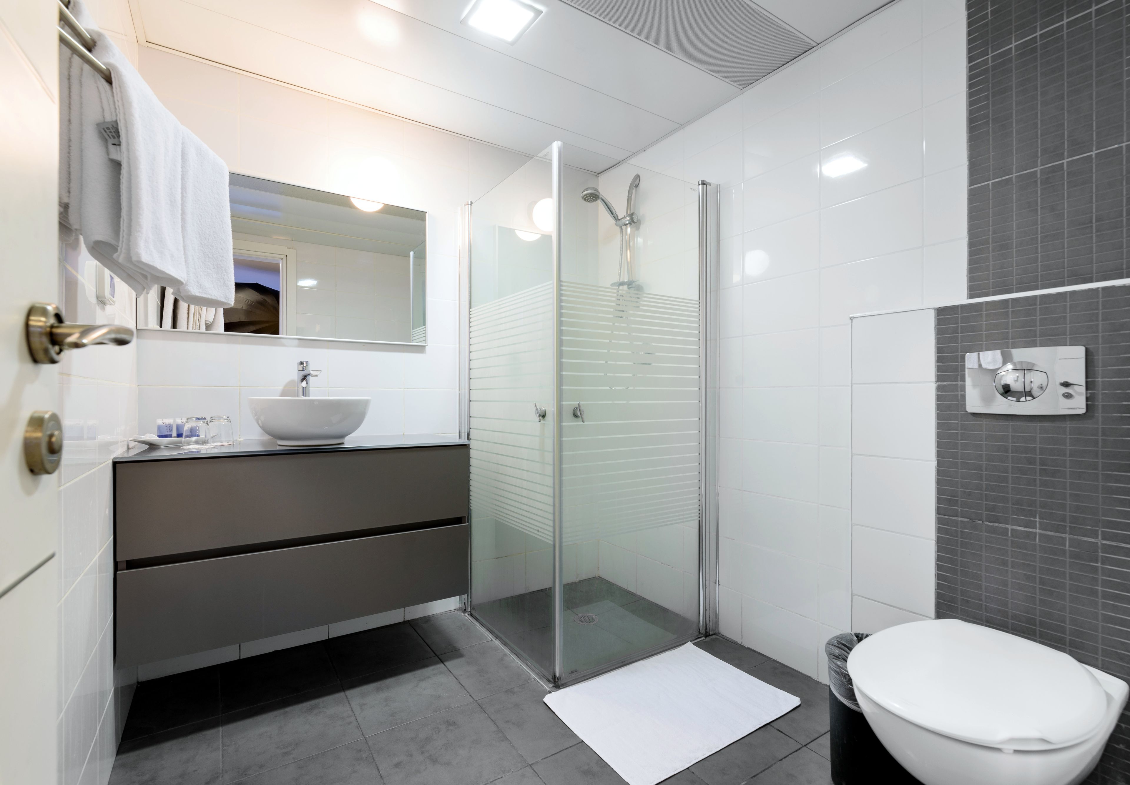 Un baño moderno con ducha acristalada, lavabo blanco y retrete.