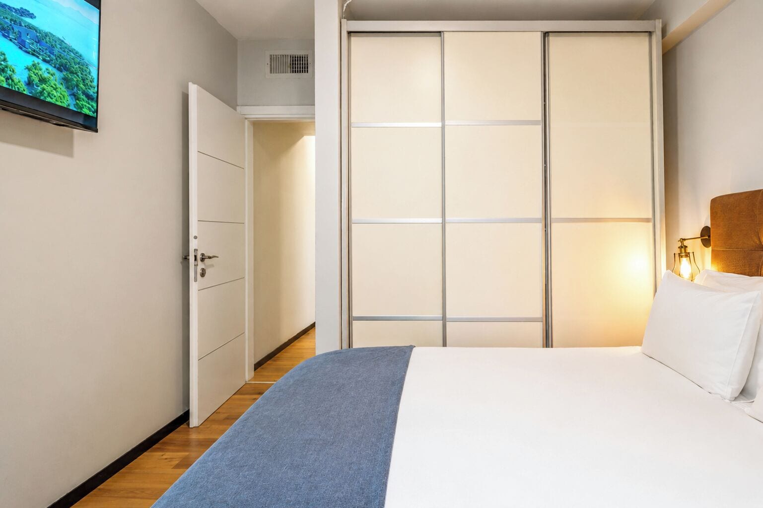 A hotel room with a bed, a wardrobe, a television, and a wall-mounted light fixture.