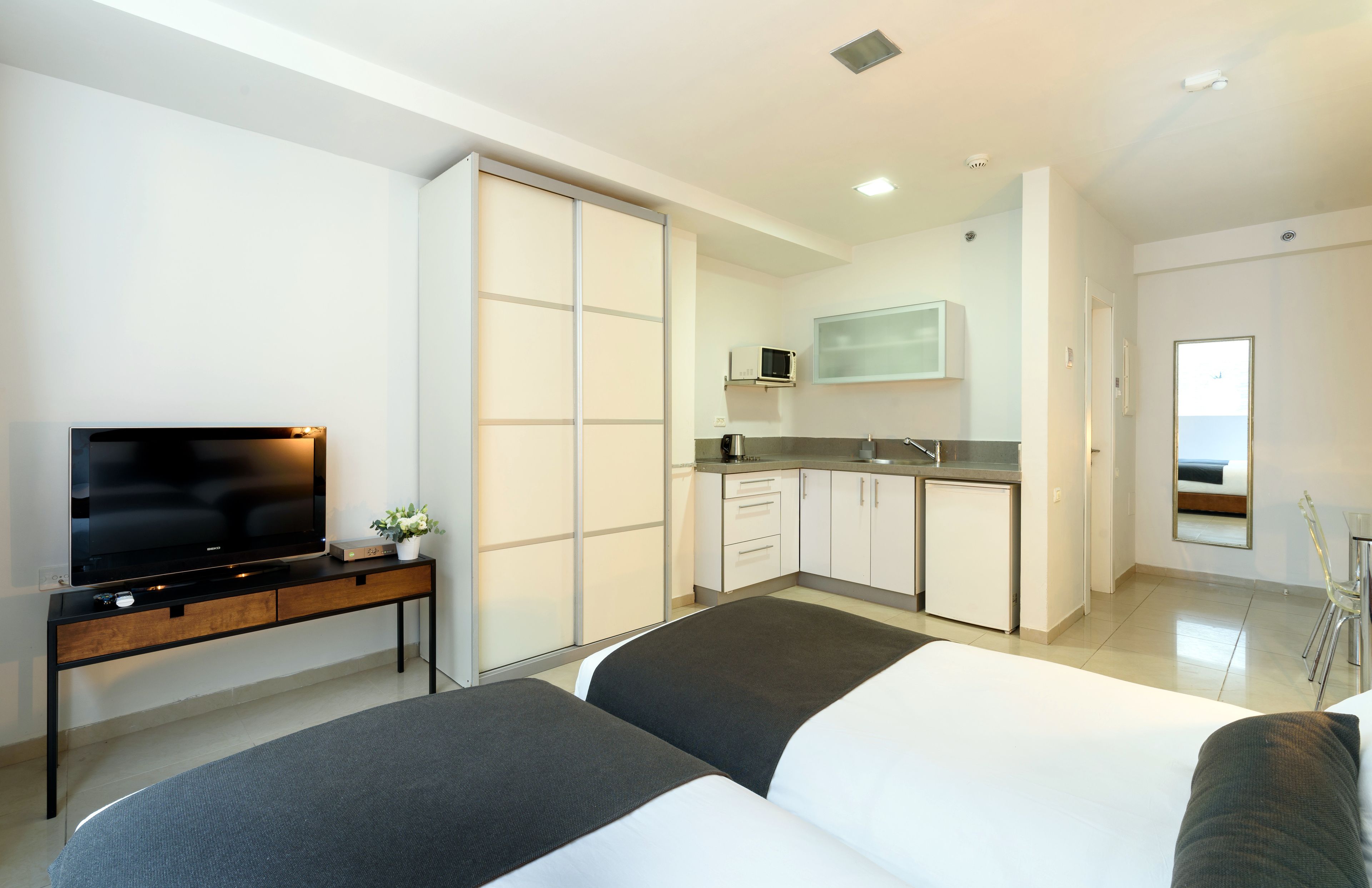 A modern hotel room with a bed, a TV, a small kitchenette, and a sliding door closet.
