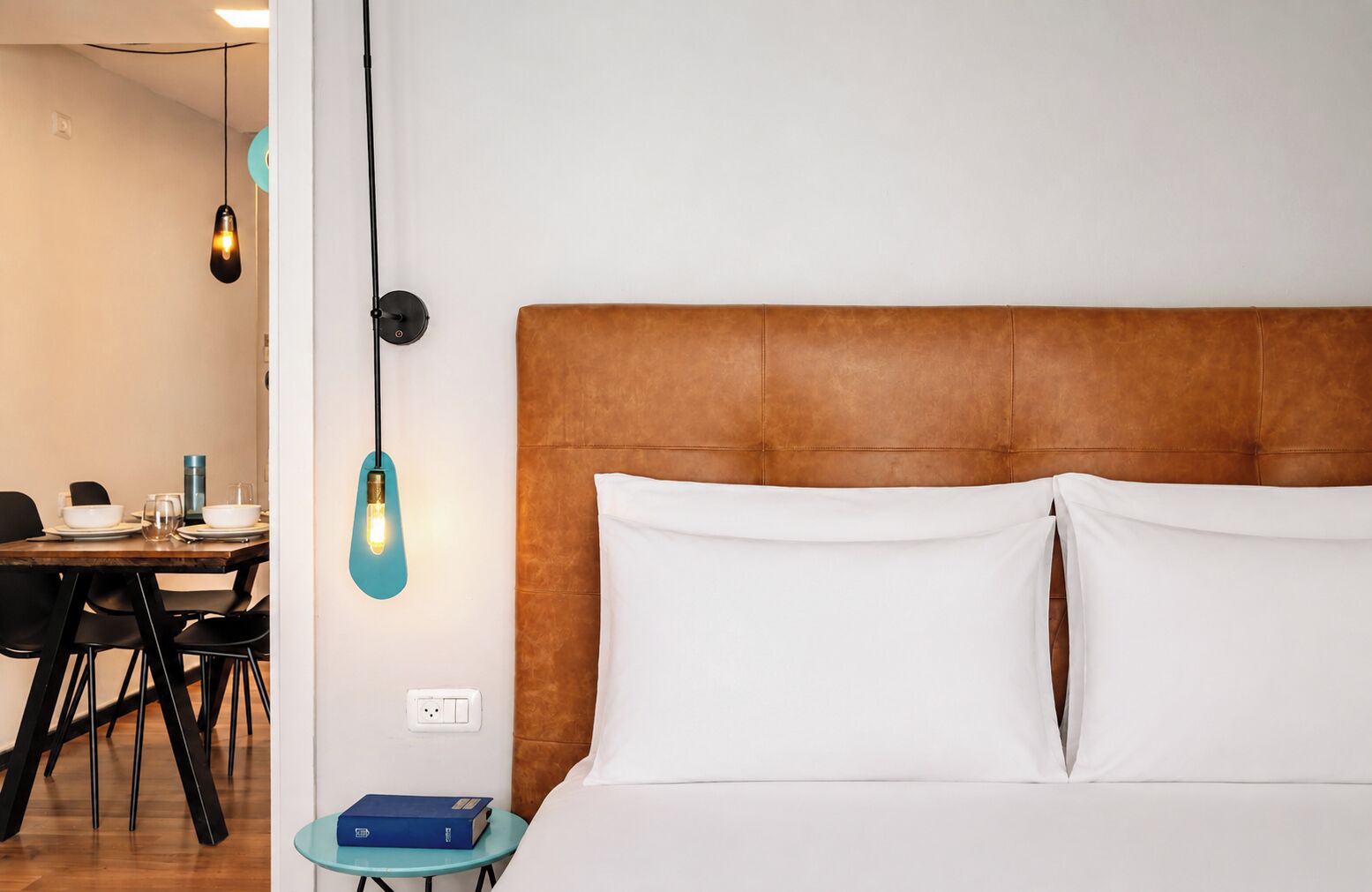 Une chambre d’hôtel comprenant un lit, une table de chevet, une table avec des chaises et des lampes suspendues.