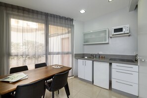 A compact kitchen with a wooden dining table, chairs, a microwave, and a sink. - Sea Land Suites - by Echo Hotels (Tel Aviv)