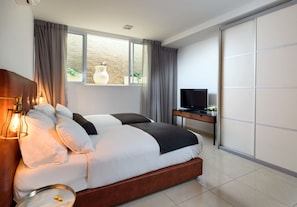 A modern bedroom with a large bed, a TV, and a sliding door. - Sea Land Suites - by Echo Hotels (Tel Aviv)