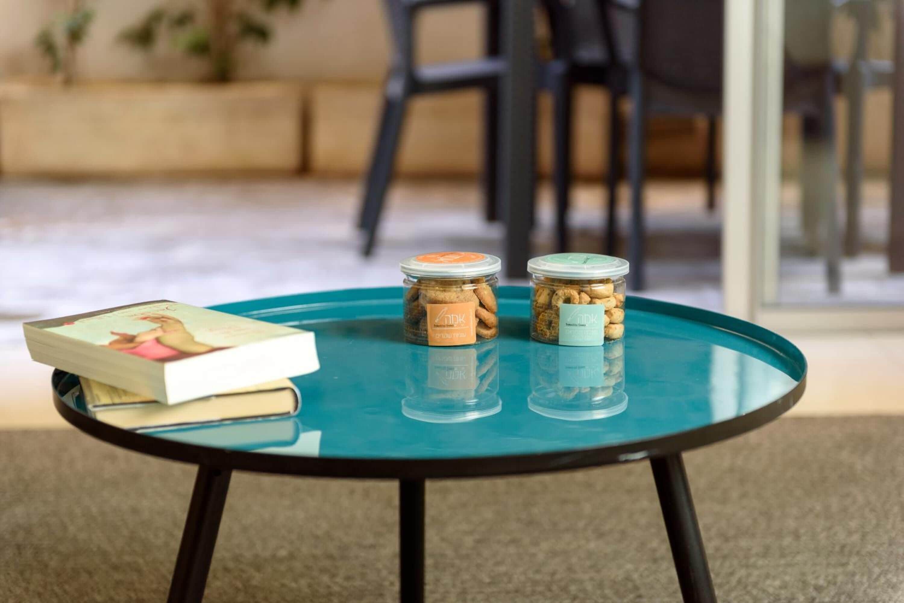A small round table with a glass top and black legs, holding a book and two jars of snacks.
