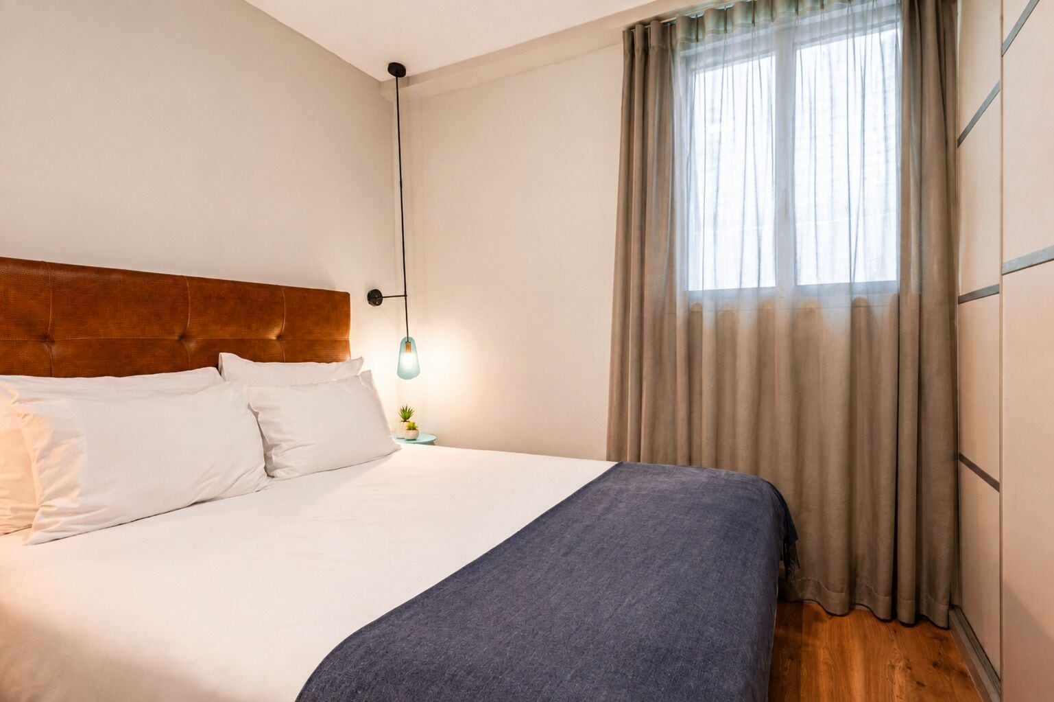 A neatly made bed with white and gray linens, a wooden headboard, and a bedside lamp.