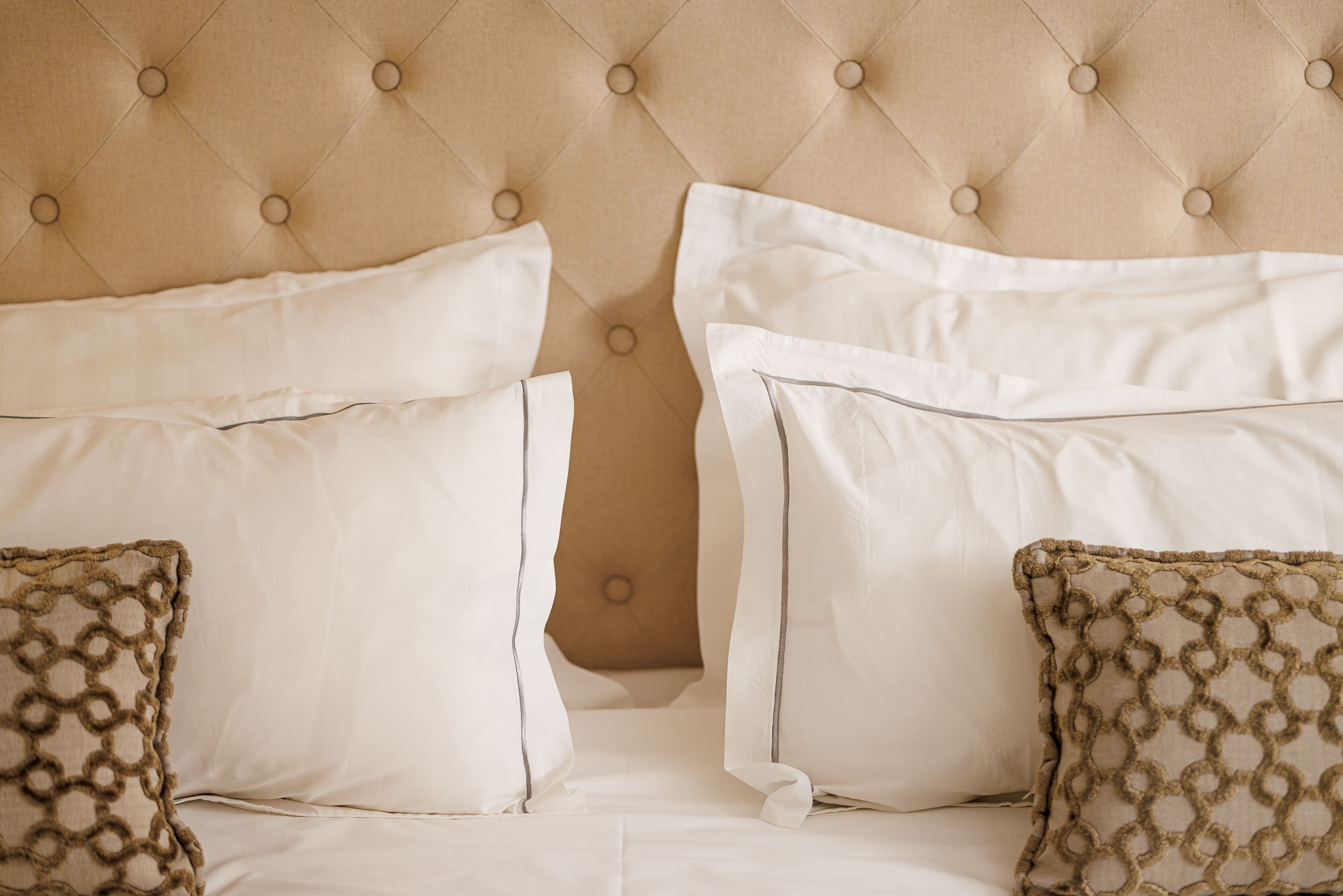 A bed with a tufted headboard, white bedding, and patterned throw pillows.