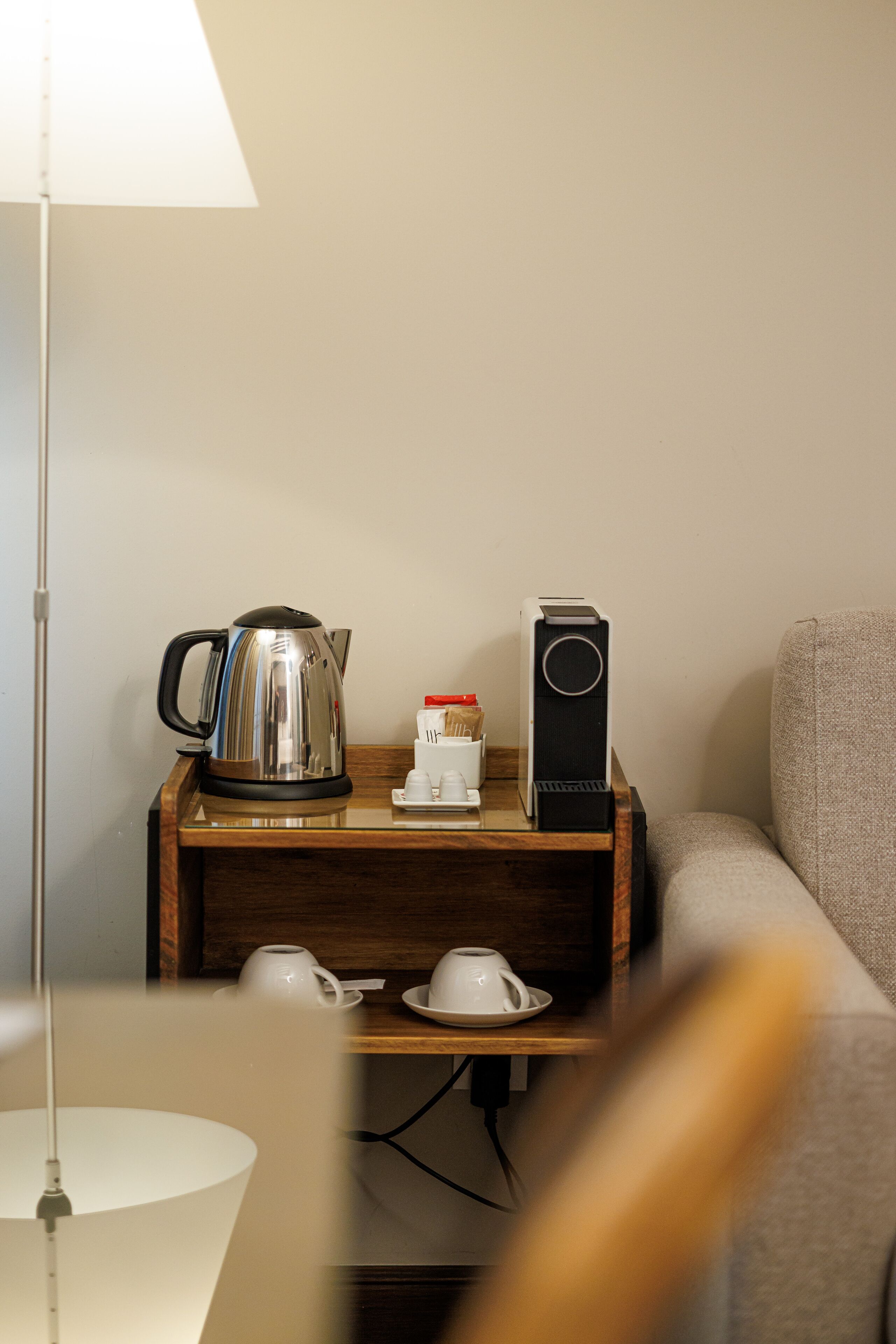 Une petite table d’appoint en bois, sur laquelle se trouvent une bouilloire, une machine à café, une tasse et une soucoupe.