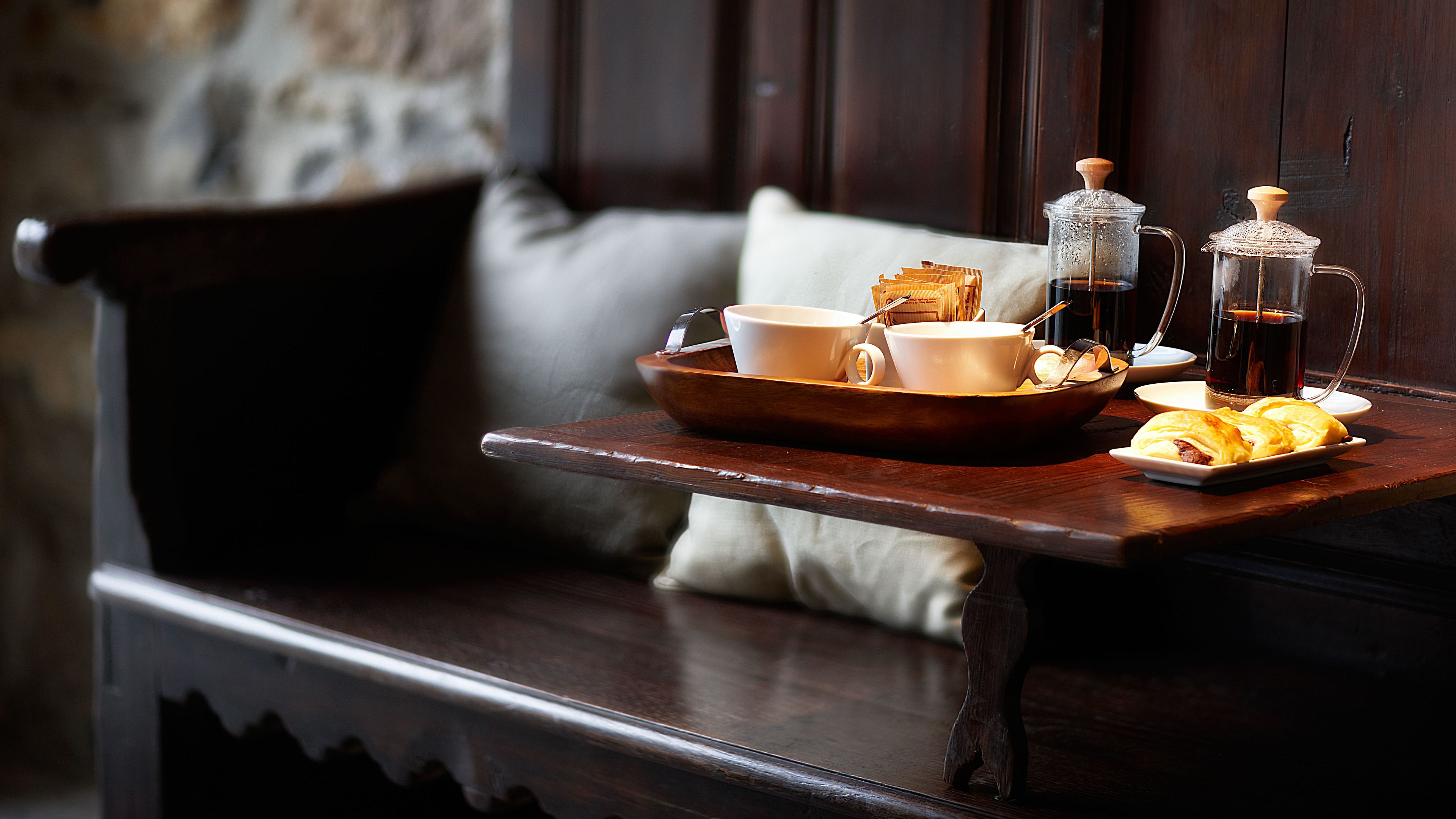 A wooden tray with a coffee pot, cups, and pastries on a table next to a bench.