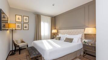 Une chambre d’hôtel bien rangée, avec un grand lit, des tables de chevet, une chaise et des tableaux encadrés accrochés au mur.