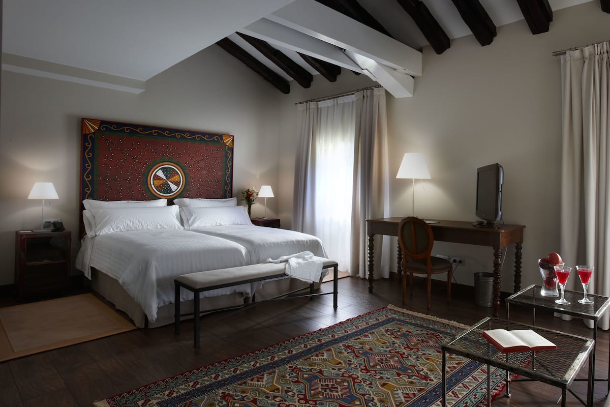 A hotel room with a large bed, a desk with a computer, a small table with a book, and a TV.