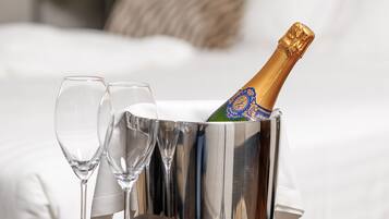 Een bed met witte lakens, een bedlampje en een fles champagne in een metalen emmer.