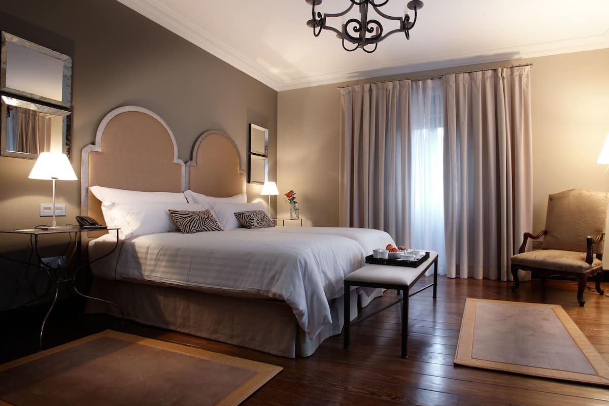 A hotel room with a large bed, bedside lamps, a chair, a desk, and a chandelier.
