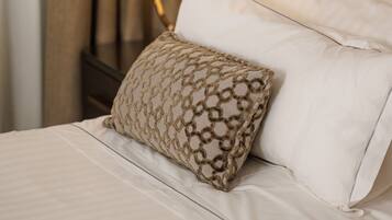 Una cama bien tendida con sábanas blancas y un cojín decorativo estampado, una lámpara de noche y un cabecero.