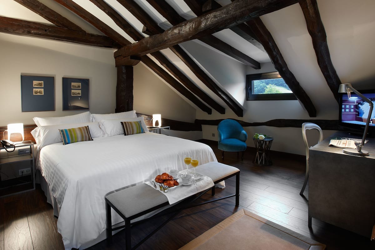 A bedroom with a large bed, bedside tables, a chair, a small table with a tray of breakfast, and a television.