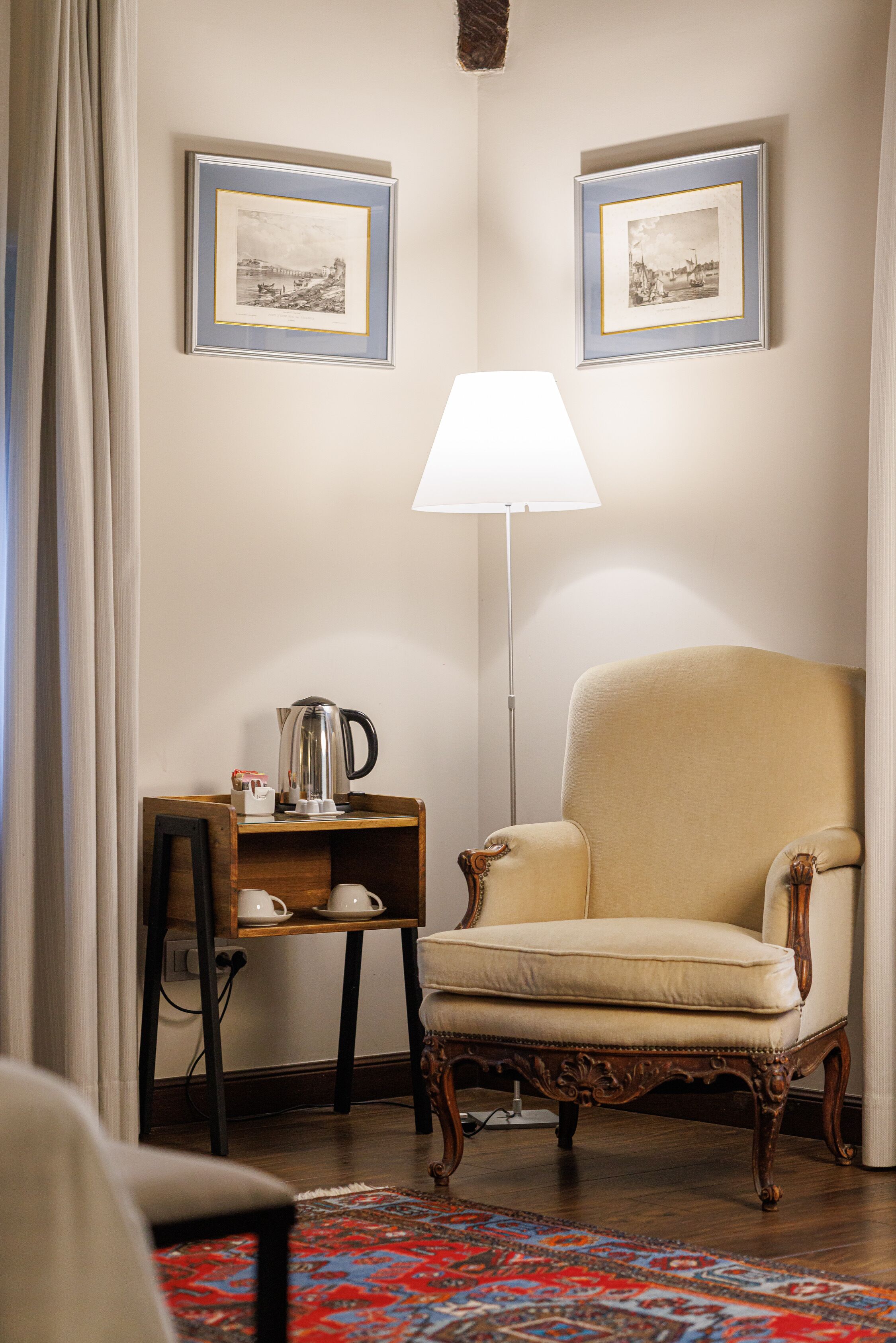Ein Zimmer mit einem großen Sessel, einem kleinen Tisch mit Wasserkocher und zwei gerahmten Bildern an der Wand.