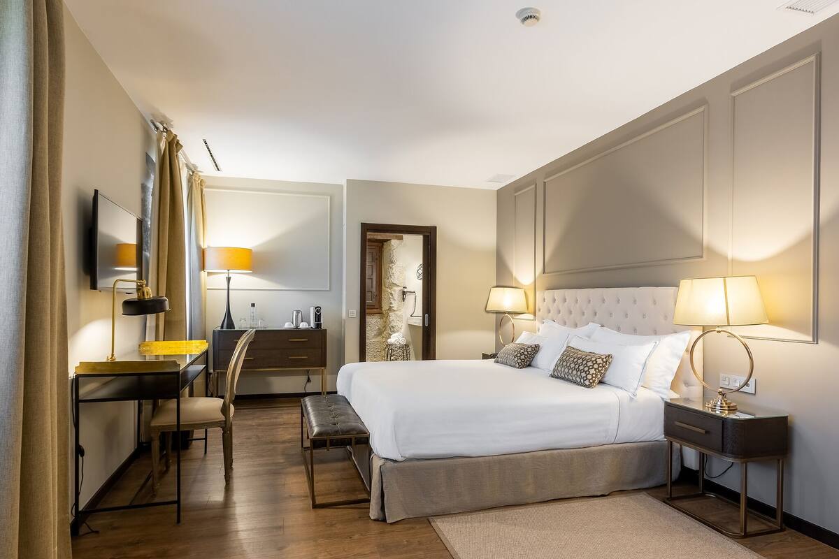 A hotel room with a bed, bedside tables, a desk, a chair, and a mirror.