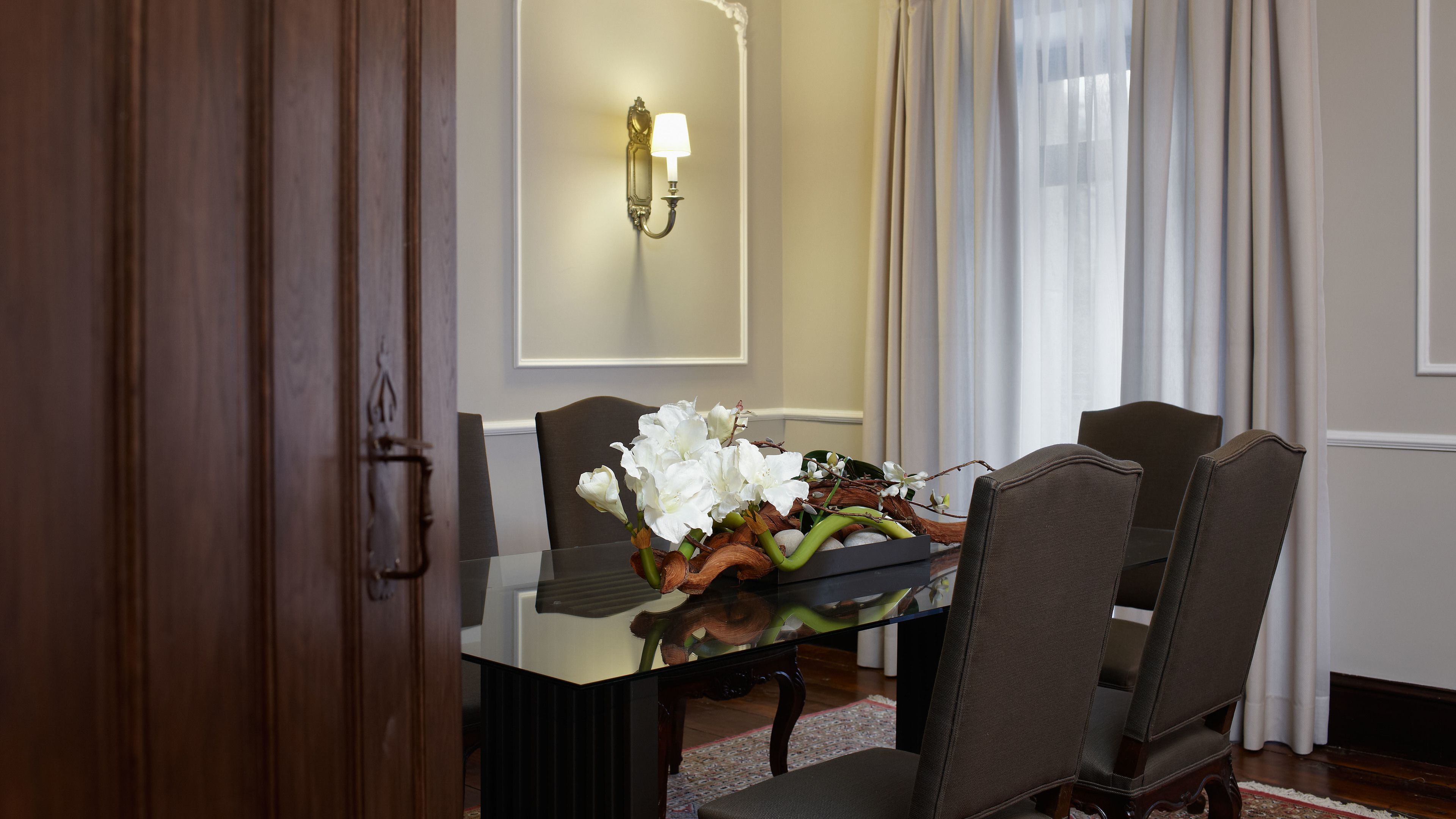 A dining area with a glass table, six chairs, and a floral centerpiece.