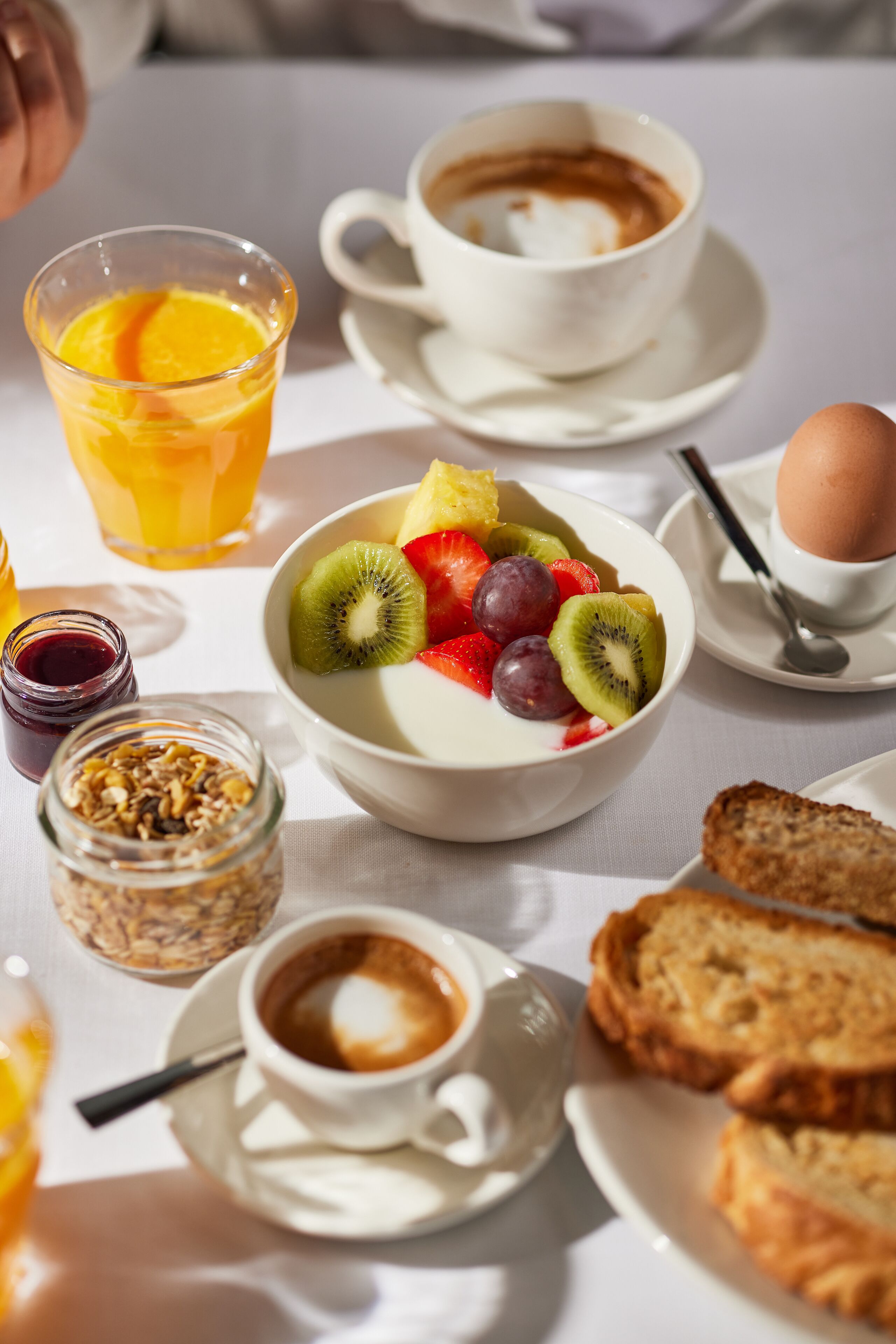 Ein Frühstückstisch mit Joghurt, Früchten, einer Tasse Kaffee, Toast und einem Glas Orangensaft.