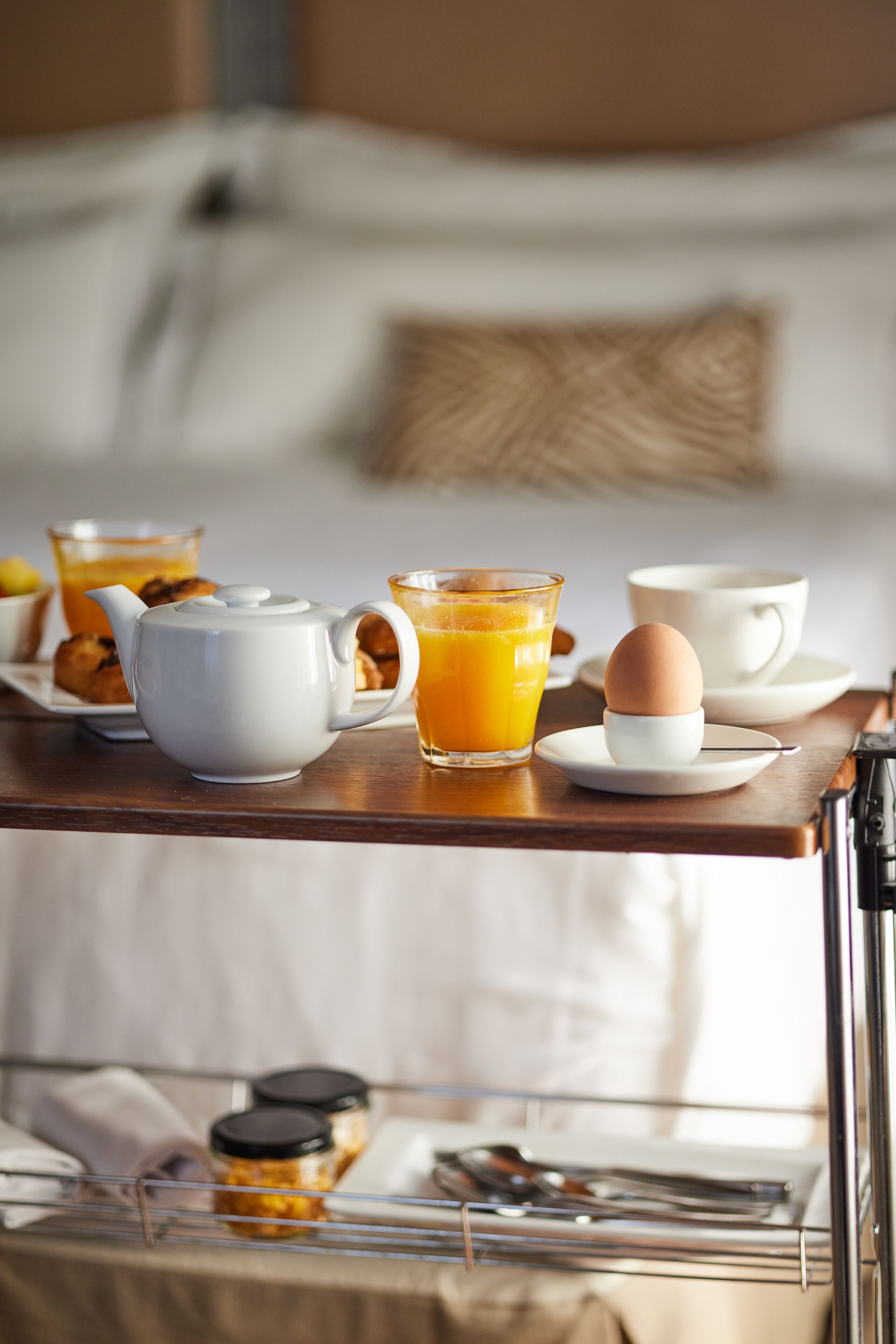 A breakfast tray with a teapot, orange juice, a cup, a plate with an egg, and a plate with pastries.