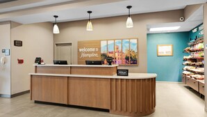 A hotel reception desk with a wooden counter, a digital clock, and a "Welcome to Hampton" sign.