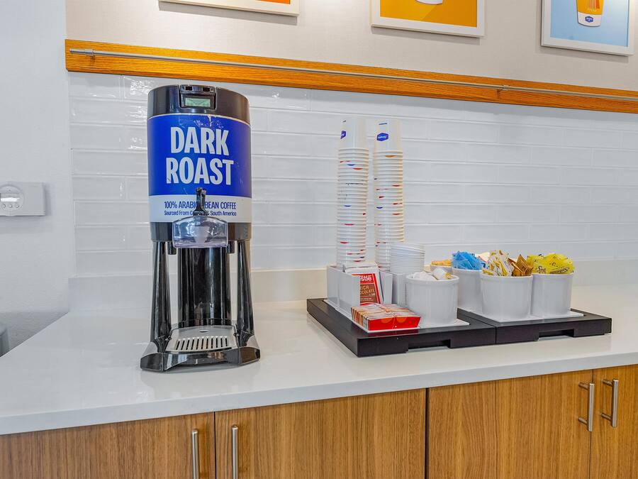 Un coin café équipé d’une machine à café sur laquelle est apposée l’étiquette « TORRÉFACTION FORTE » et d’une pile de gobelets jetables.