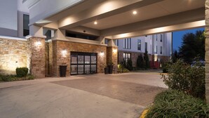 A hotel entrance with stone facade, glass doors, and outdoor seating.