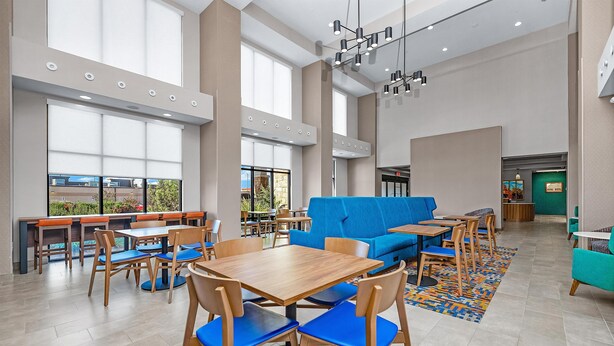 A spacious indoor area with multiple tables and chairs, a blue sofa, and large windows allowing natural light.