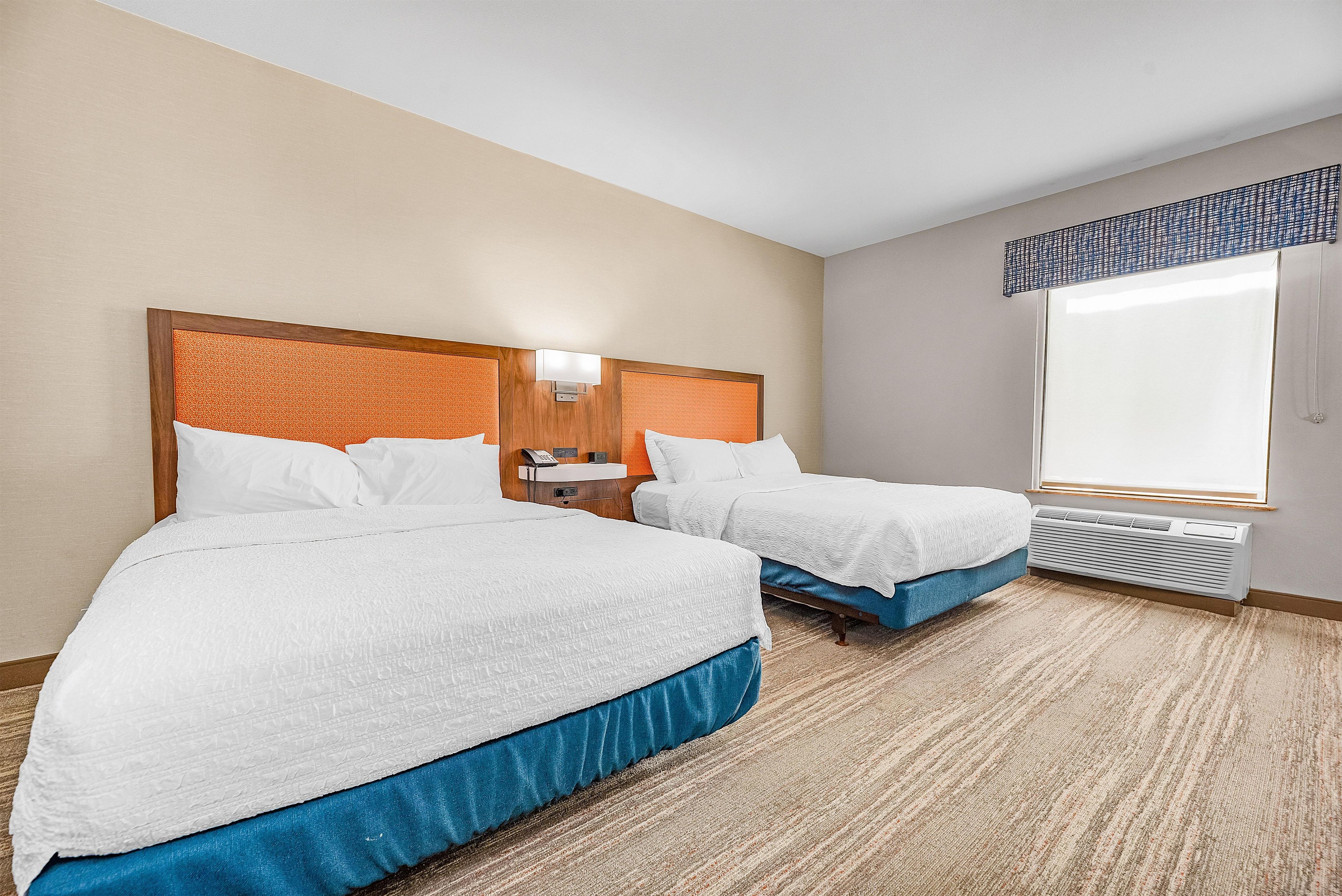 Une chambre d’hôtel avec deux lits, une table de chevet, un téléphone et une fenêtre donnant sur un paysage agréable.