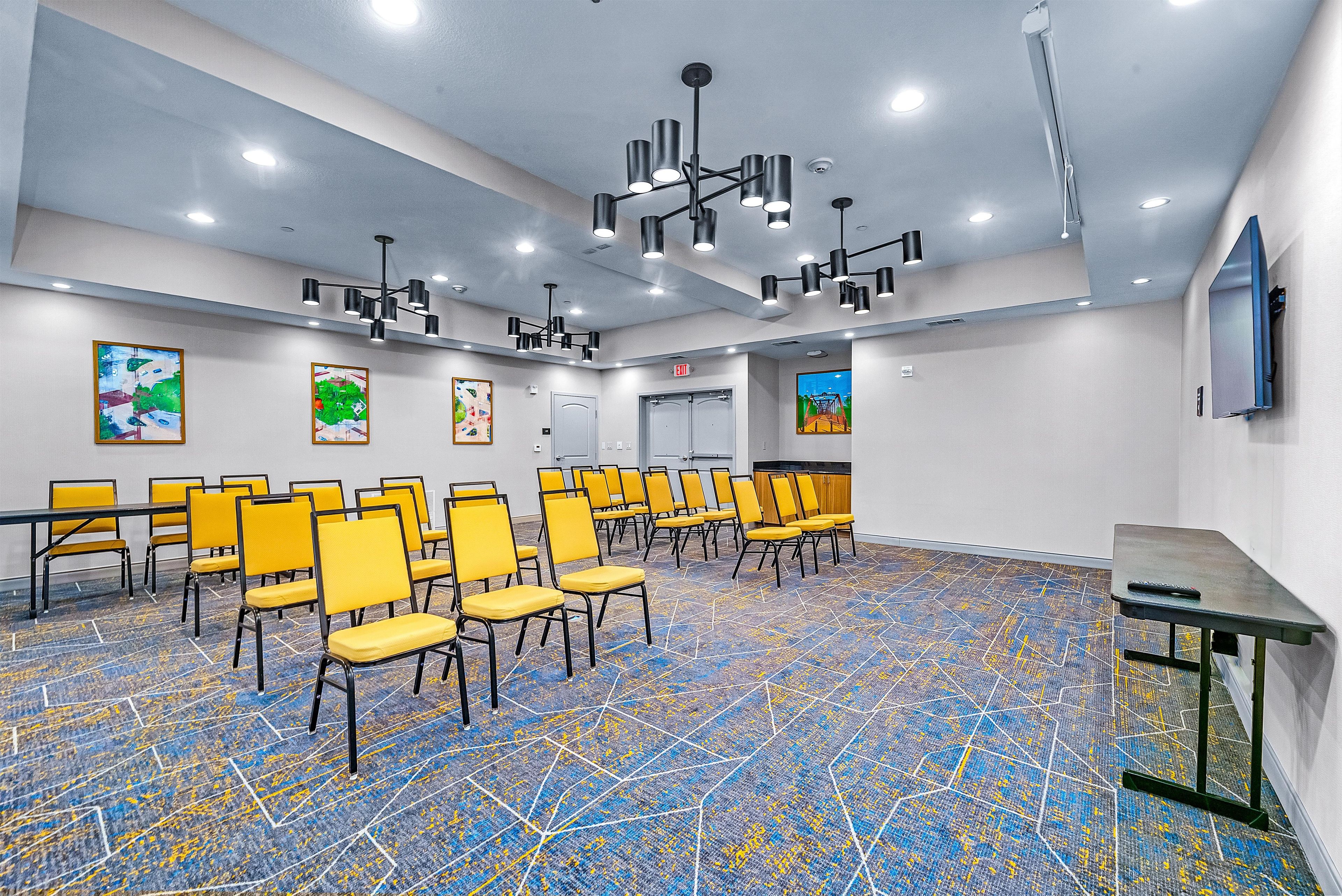 A conference room with rows of yellow chairs, a blue and yellow patterned carpet, and multiple ceiling lights.