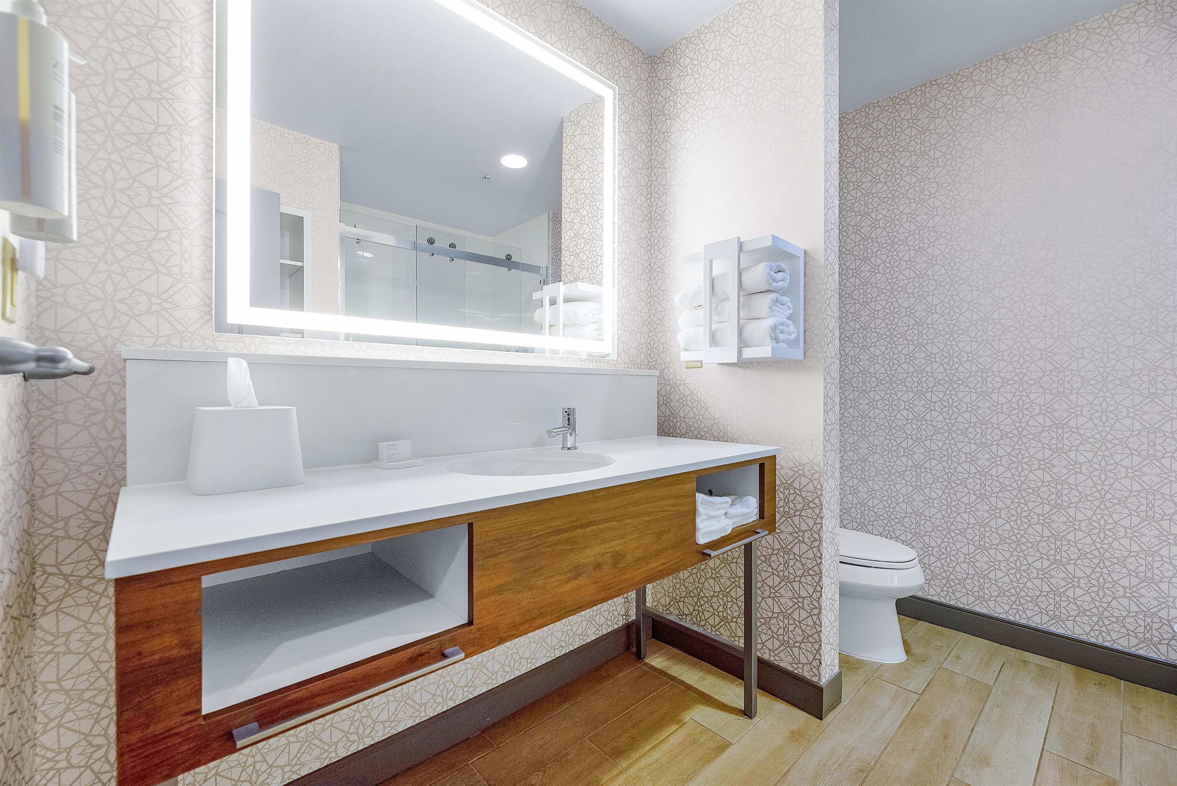 A modern bathroom with a large mirror, white sink, wooden vanity, and a toilet.