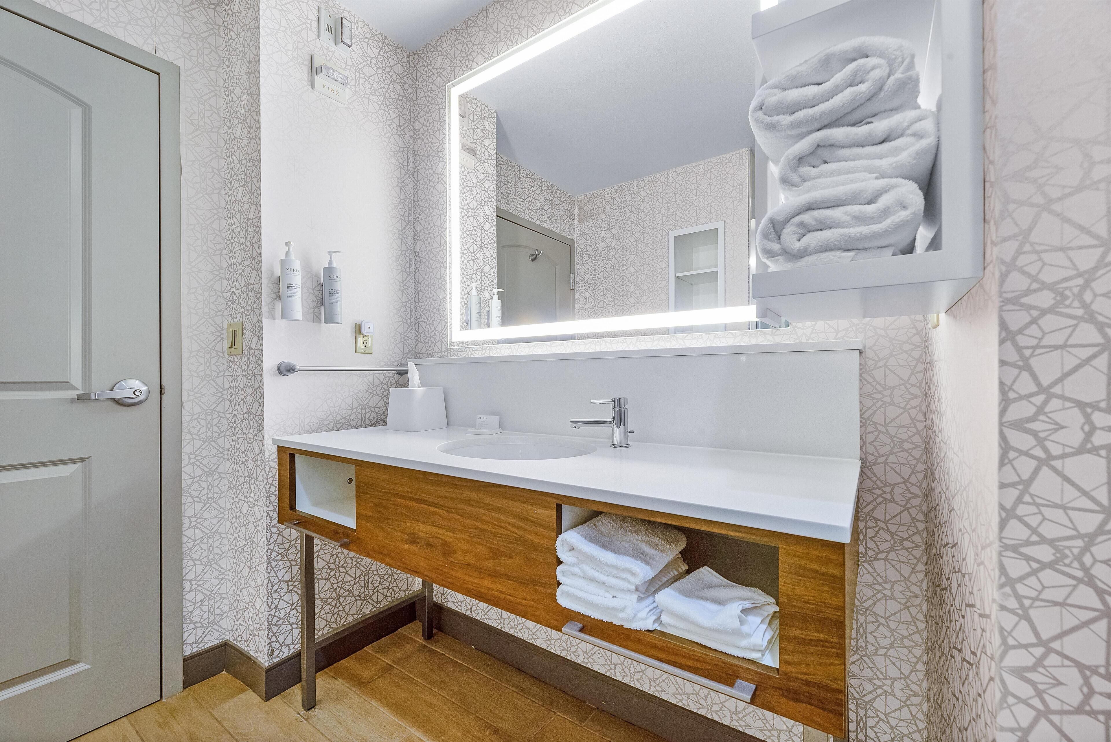 A modern bathroom with a white vanity, a large mirror, and neatly folded towels.