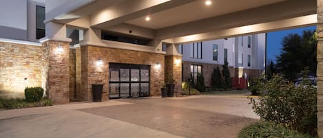 A hotel entrance with stone facade, glass doors, and a covered walkway.
