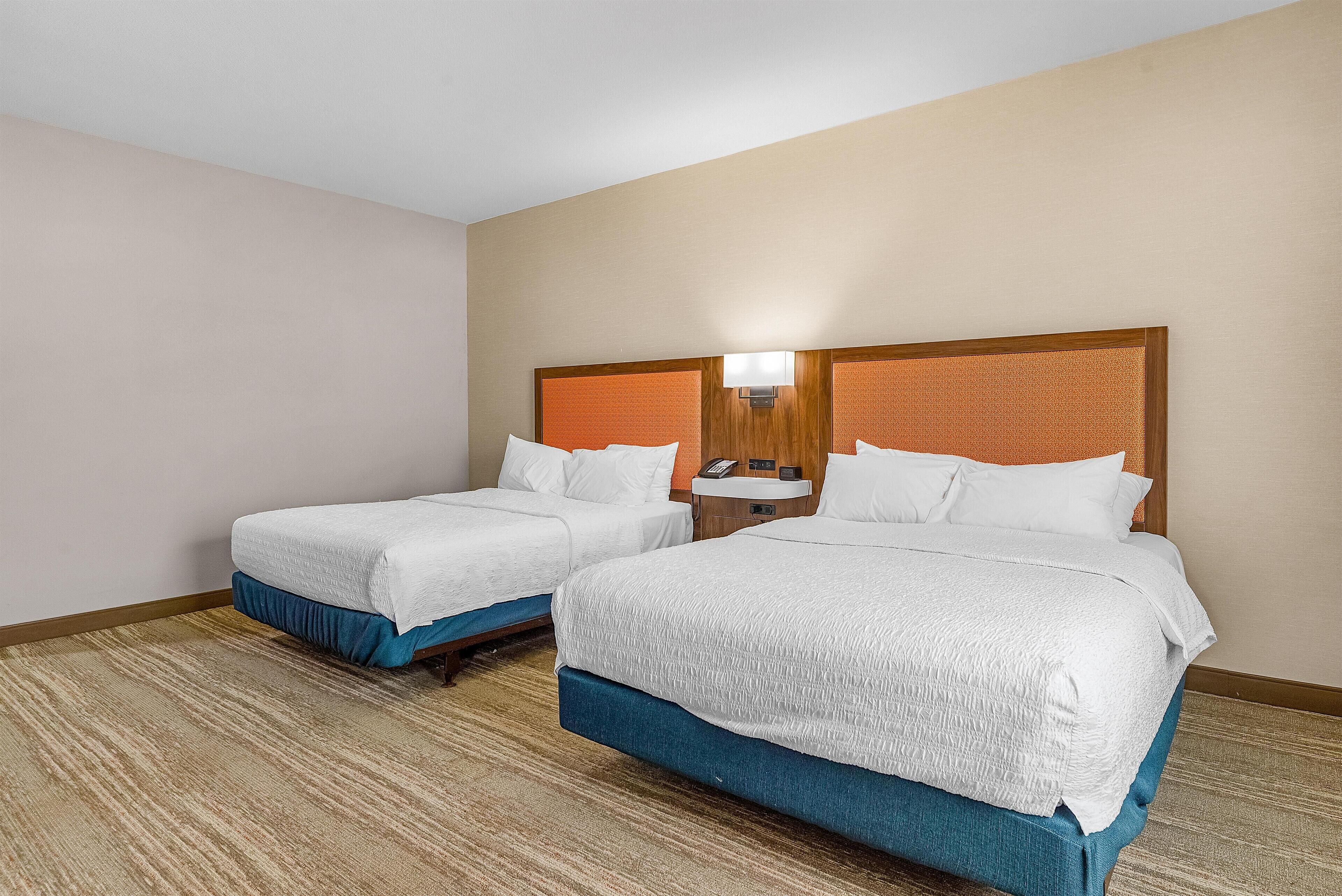 A hotel room with two beds, a nightstand with a lamp, and a telephone.