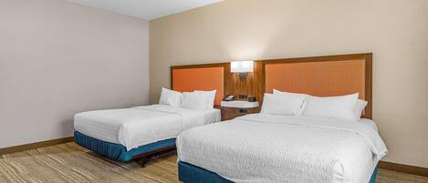 A hotel room with two beds, a nightstand with a lamp, and a telephone.
