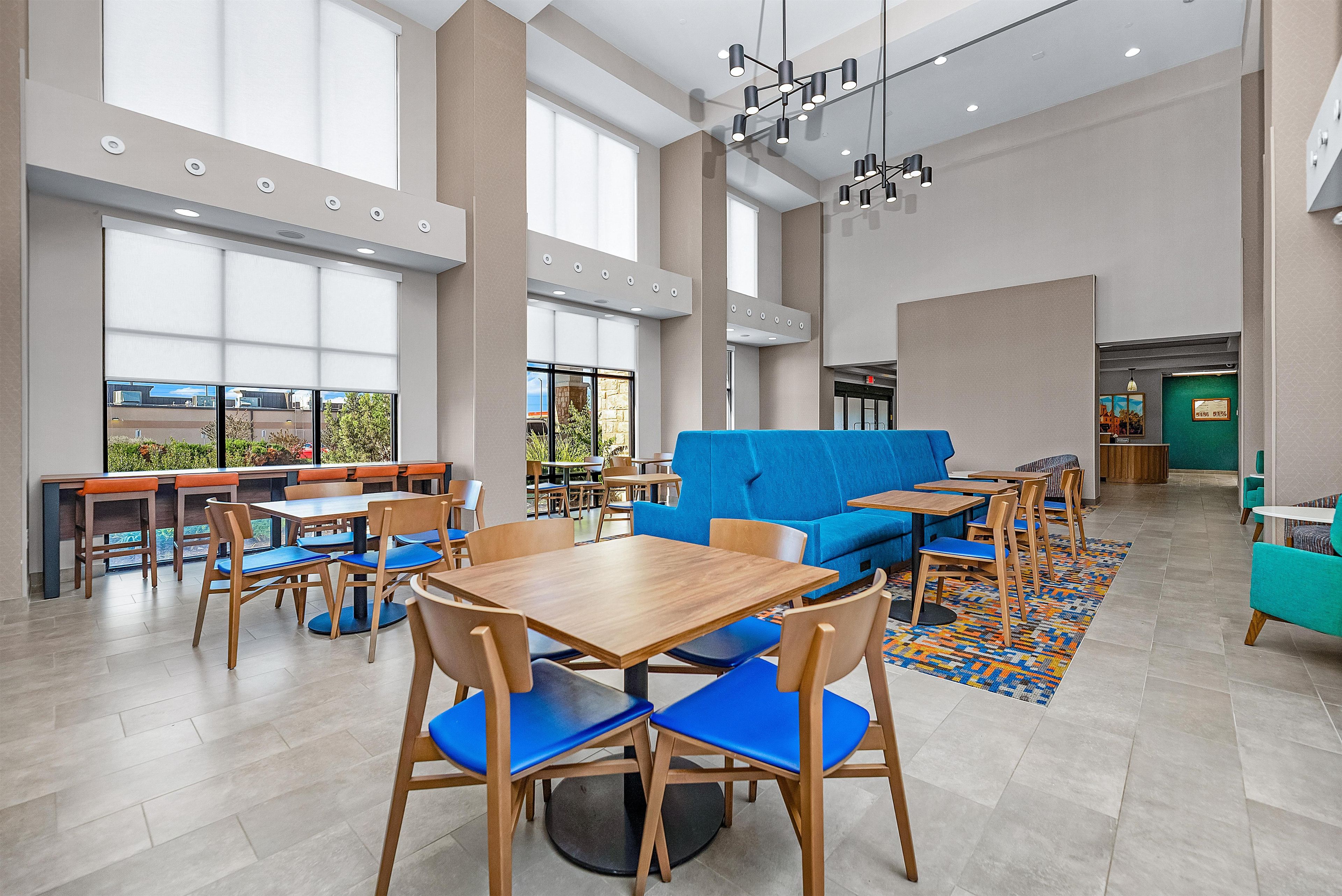 A spacious indoor area with multiple seating arrangements including tables and chairs, a blue sofa, and a patterned rug on the floor.