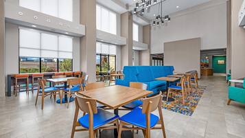 A spacious indoor area with multiple seating arrangements including tables and chairs, a blue sofa, and a patterned rug on the floor.