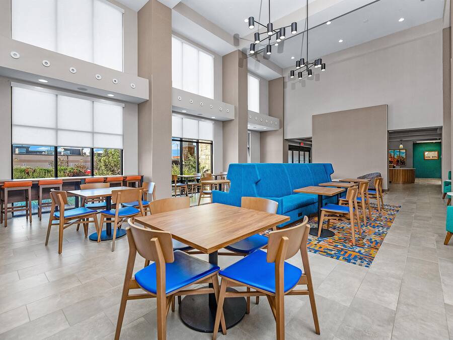 A spacious indoor area with multiple seating arrangements including tables and chairs, a blue sofa, and a patterned rug on the floor.