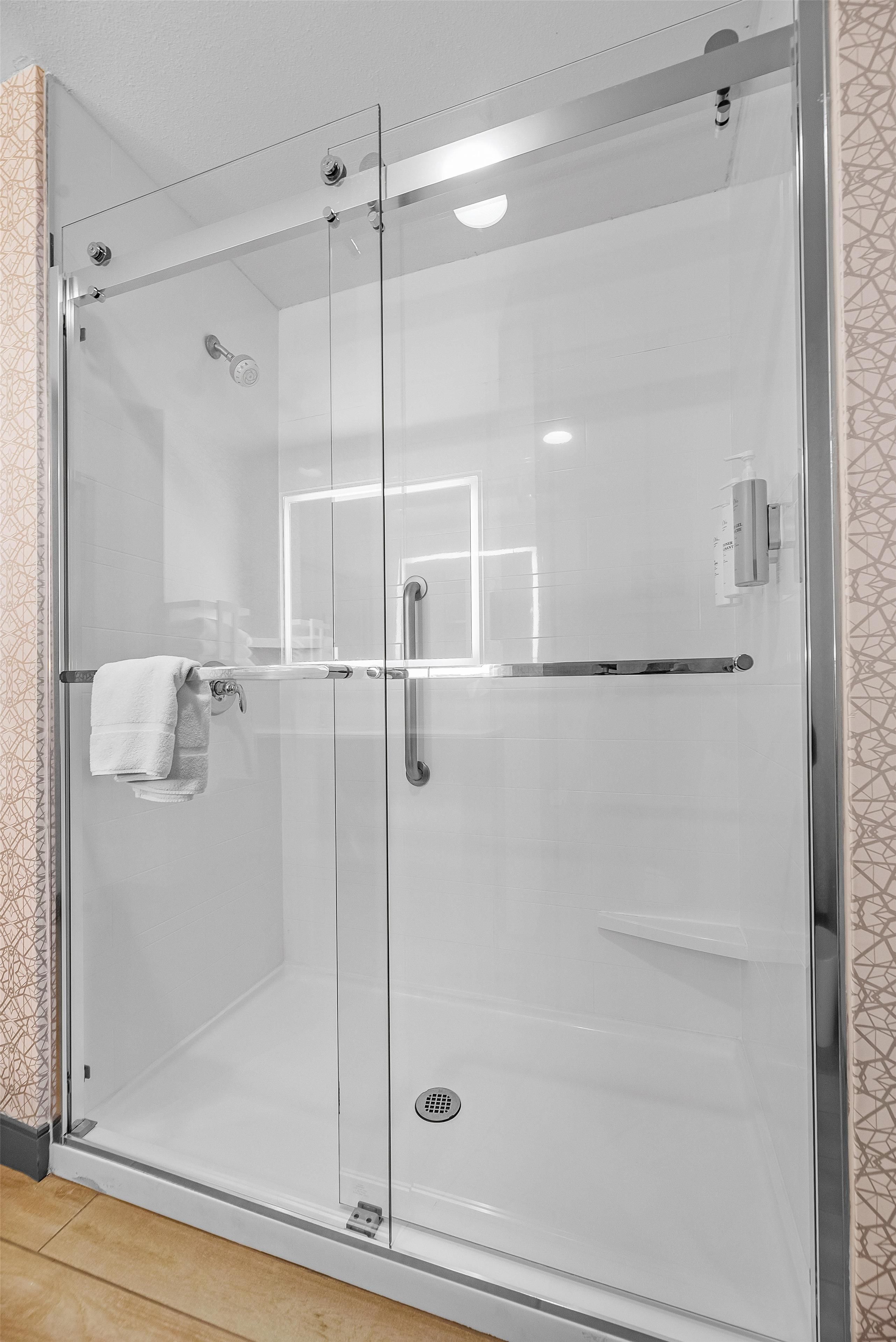 A glass-enclosed shower stall with a towel rack and a control panel.
