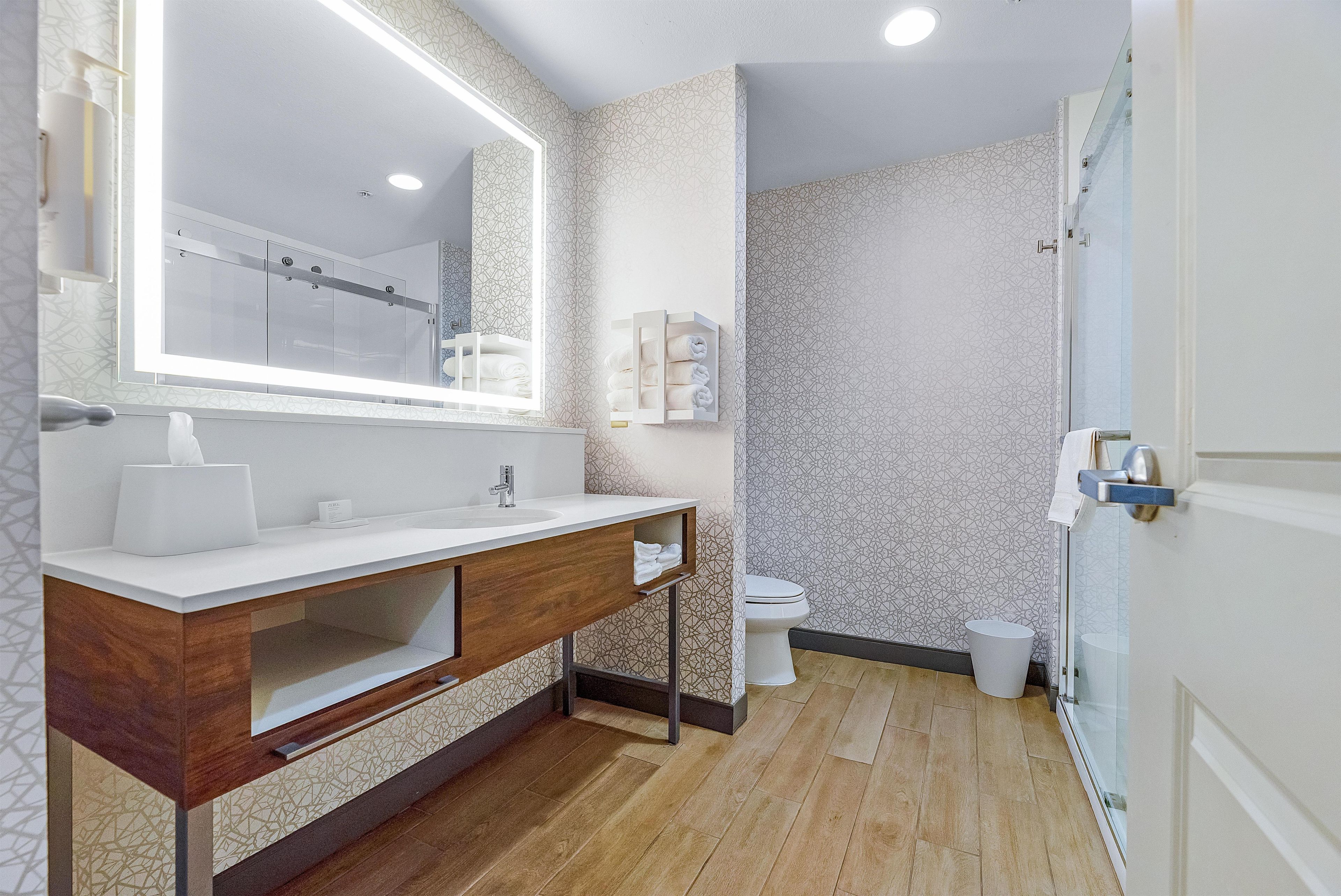 Une salle de bain moderne avec un meuble-lavabo en bois, un grand miroir et un espace douche.