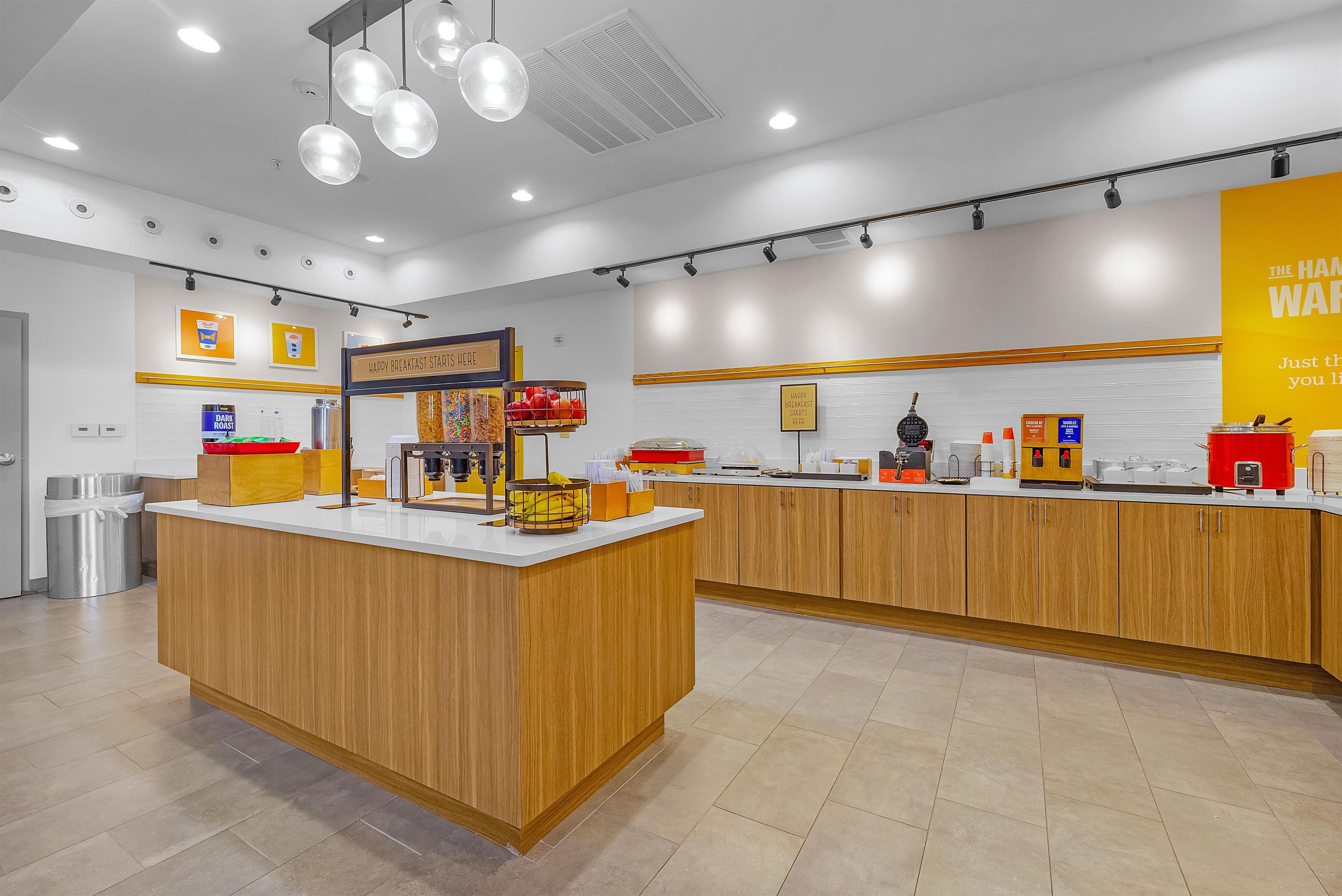 A breakfast area with a wooden counter, a sign that reads 'HAPPY BREAKFAST STARTS HERE', and various breakfast items displayed.