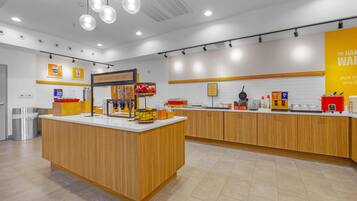 A breakfast area with a wooden counter, a sign that reads 'HAPPY BREAKFAST STARTS HERE', and various breakfast items displayed.