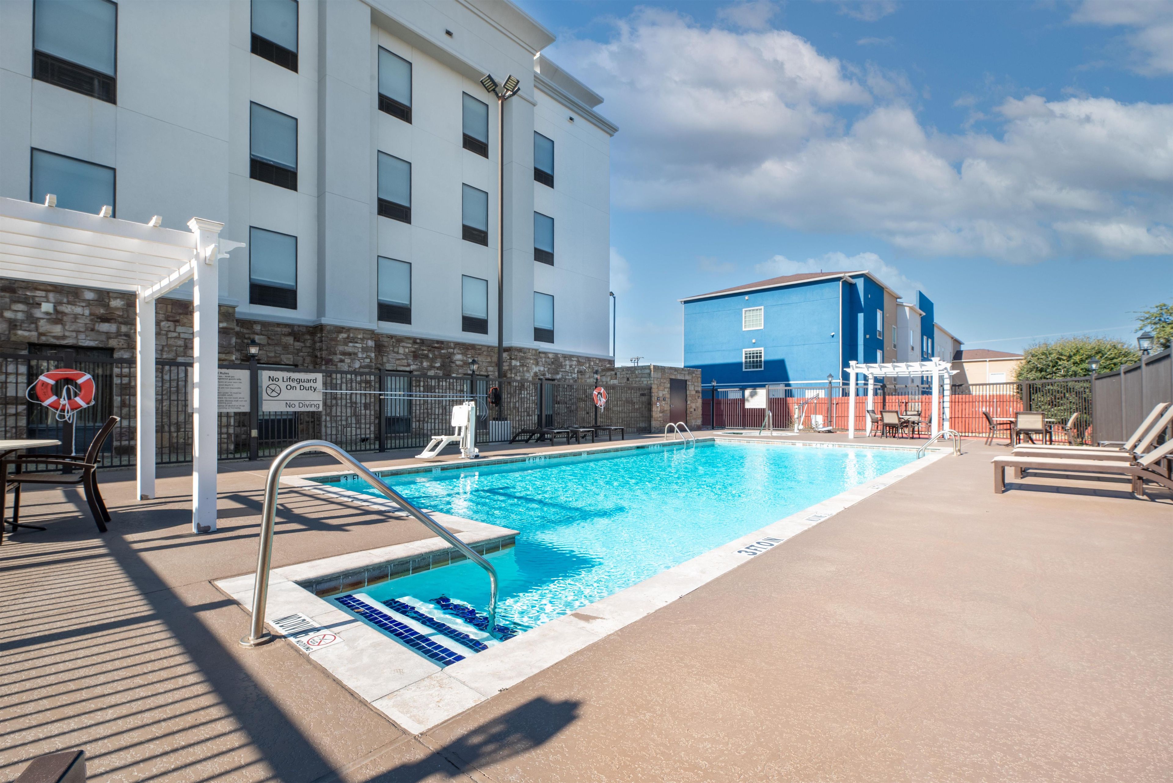 A swimming pool with a lifeguard stand, a no diving sign, and a no lifeguard on duty sign.