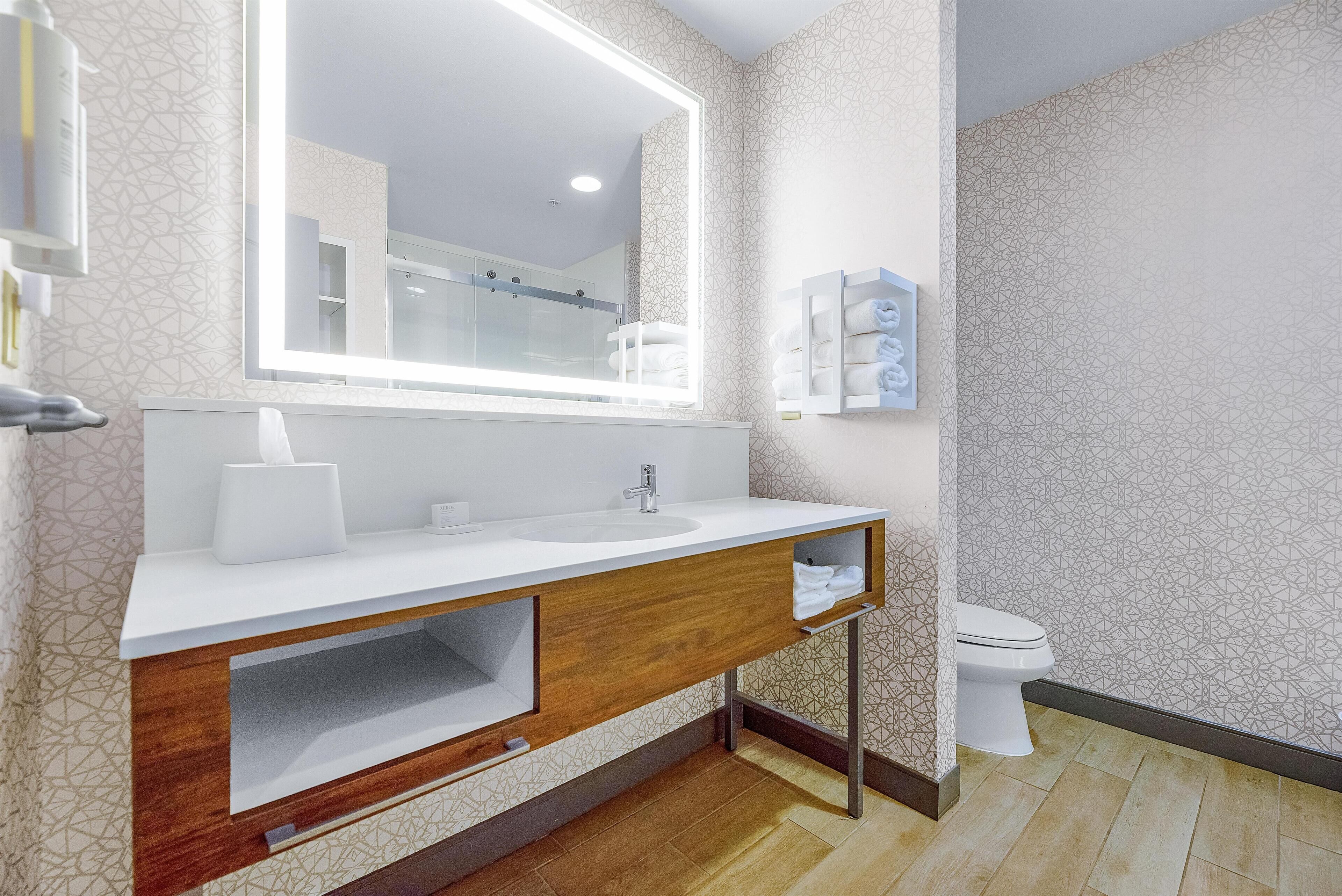 Un baño moderno con un tocador blanco, un espejo grande y un inodoro.